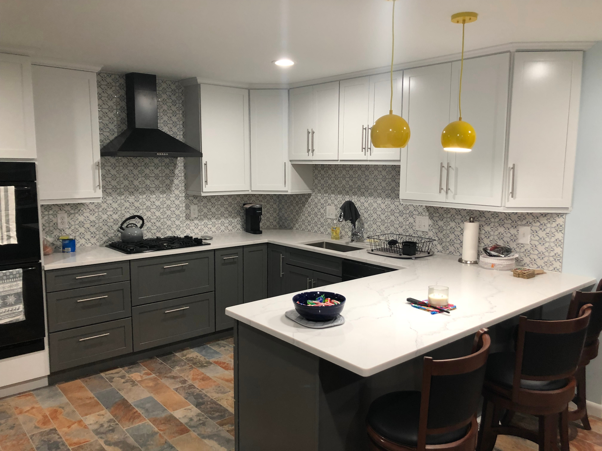 Two-tone kitchen with patterned tile backsplash and yellow pendants